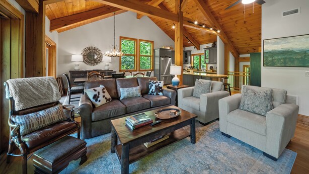 A spacious living room with a high ceiling, wooden beams, a fireplace, a dining area, and large windows. - Muir Lodge (Blowing Rock)