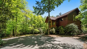 A cabin surrounded by dense forest with a paved driveway leading to the entrance. - Muir Lodge (Blowing Rock)