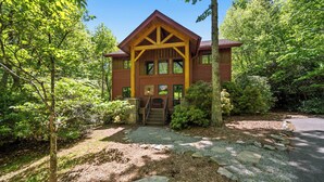 Une cabane en bois dotée d’un porche, entourée d’arbres et bordée d’une allée en gravier.