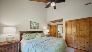 Une chambre à coucher comprenant un lit, une armoire en bois, des tables de chevet et un ventilateur de plafond.