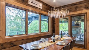 A wooden dining area with a large table set for six, a chandelier, and a view of the outdoors. - Ambience Lodge at Eagles Nest (Banner Elk)