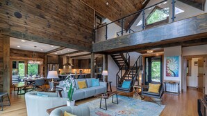 A spacious living area with a high ceiling, wooden beams, a large sofa set, a dining table, and a staircase leading to an upper level. - Ambience Lodge at Eagles Nest (Banner Elk)