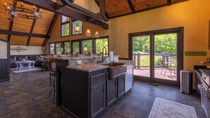 A spacious kitchen with dark cabinetry, a large island, and a view to an outdoor patio. - Halftime Haus (Banner Elk)