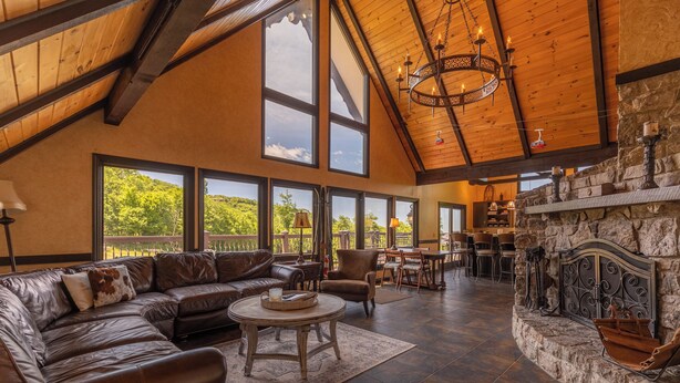 A spacious living room with a large leather sectional sofa, a round coffee table, and a stone fireplace. - Halftime Haus (Banner Elk)