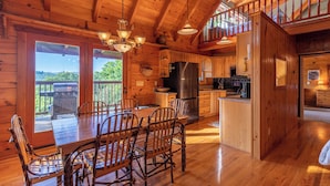 A wooden cabin interior with a dining area, kitchen, and a balcony with a grill. - Whispering Ridge Retreat (Boone)