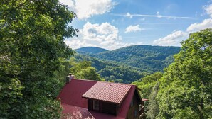 A cabin with a red roof nestled among lush green trees, overlooking a forested valley. - Whispering Ridge Retreat (Boone)