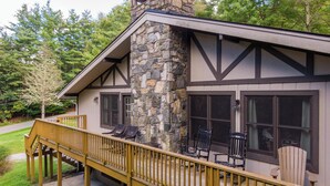 Un chalet doté d’une cheminée en pierre, d’une terrasse en bois et d’une grande fenêtre.