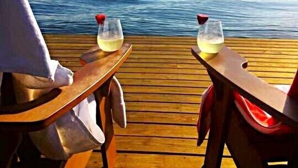 A wooden deck with two tables, each with a glass of white wine and a red napkin.