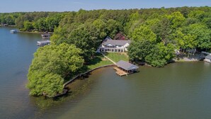 A large house surrounded by dense forest, connected to a dock, and situated on a lake.