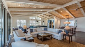 A spacious living area with a high ceiling, a large sofa set, a dining table, and a kitchen in the background.