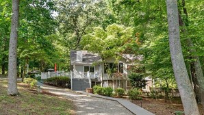 A two-story house with a porch, surrounded by trees and a gravel path. - Lake Relaxin` | Fabulous Flat Lot | Great Water View! (Henrico)