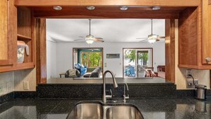 A kitchen with a double sink, wooden cabinets, and a view of a living area with a blue sofa and a dining table. - Lake Relaxin` | Fabulous Flat Lot | Great Water View! (Henrico)