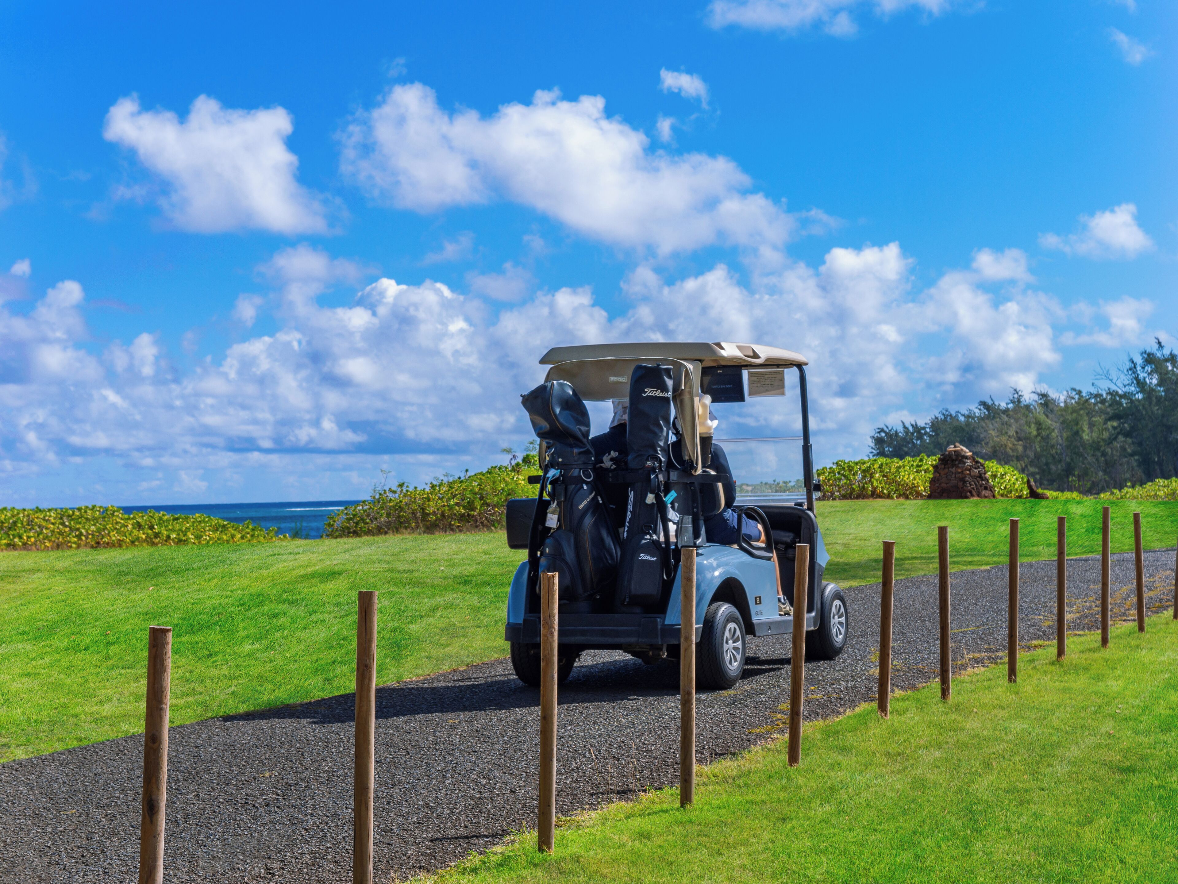 Ein Golfmobil auf einem Kiesweg mit Blick auf das Meer und einen klaren Himmel.