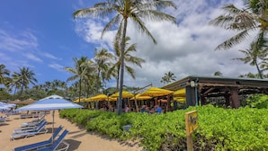 A beachside restaurant with outdoor seating, palm trees, and a sandy beach.
