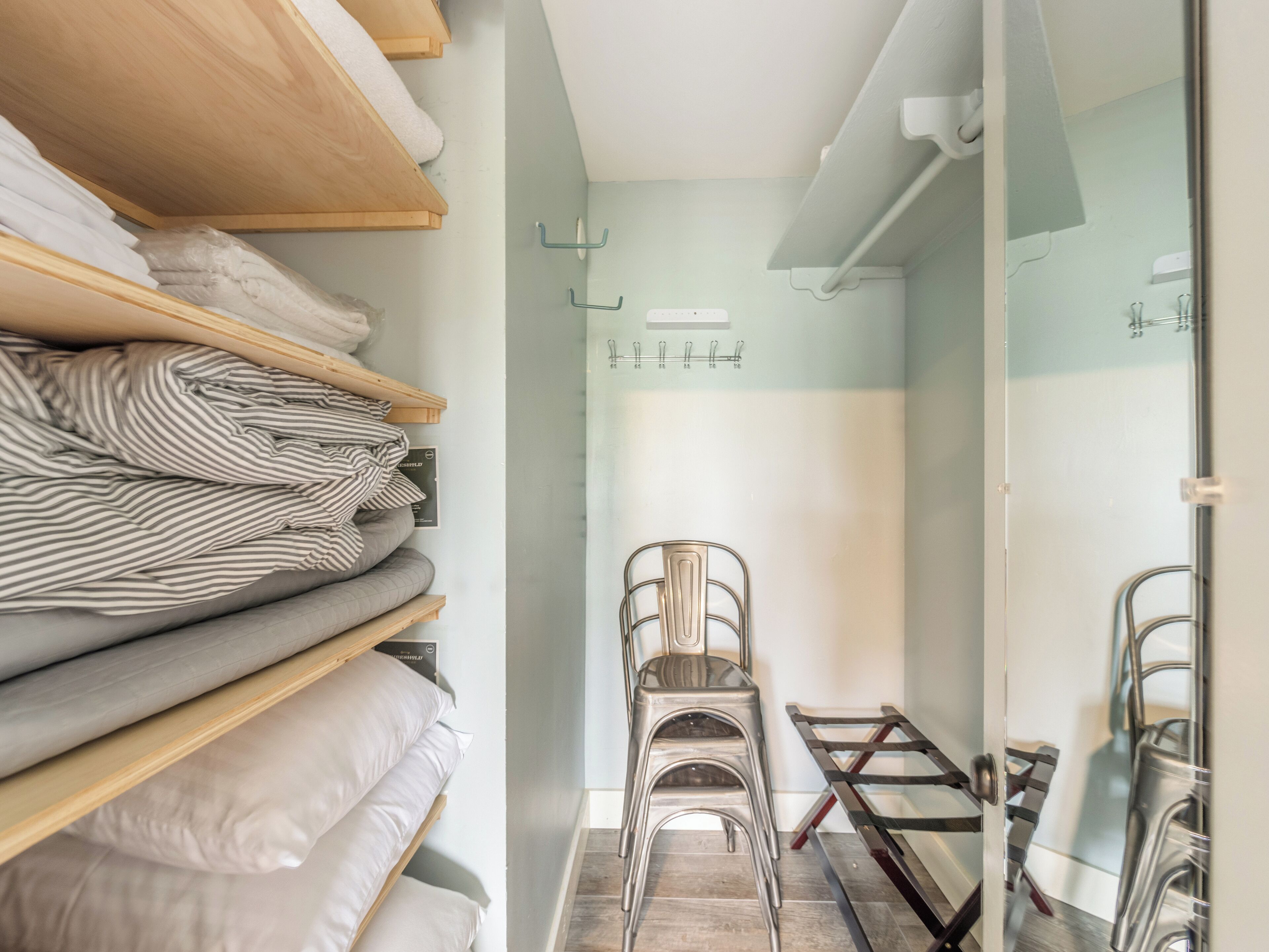 Un placard de rangement avec des étagères où sont pliés le linge de lit, et un tabouret en métal.