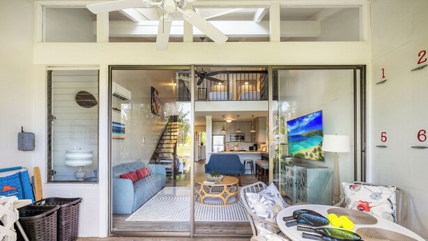 A spacious living area with a large glass door leading to a kitchen and upper floor.