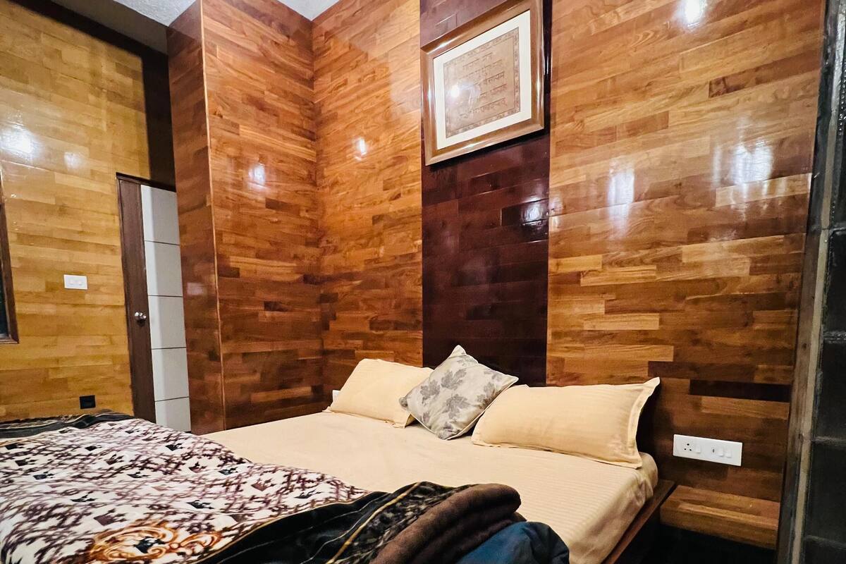 Une chambre avec un mur décoré de panneaux en bois, un lit recouvert d’une courtepointe à motifs et un tableau encadré au-dessus du lit.