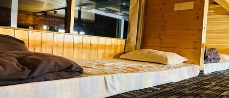 Una habitación de cabaña de madera con dos camas, una ventana y una lámpara en el techo.