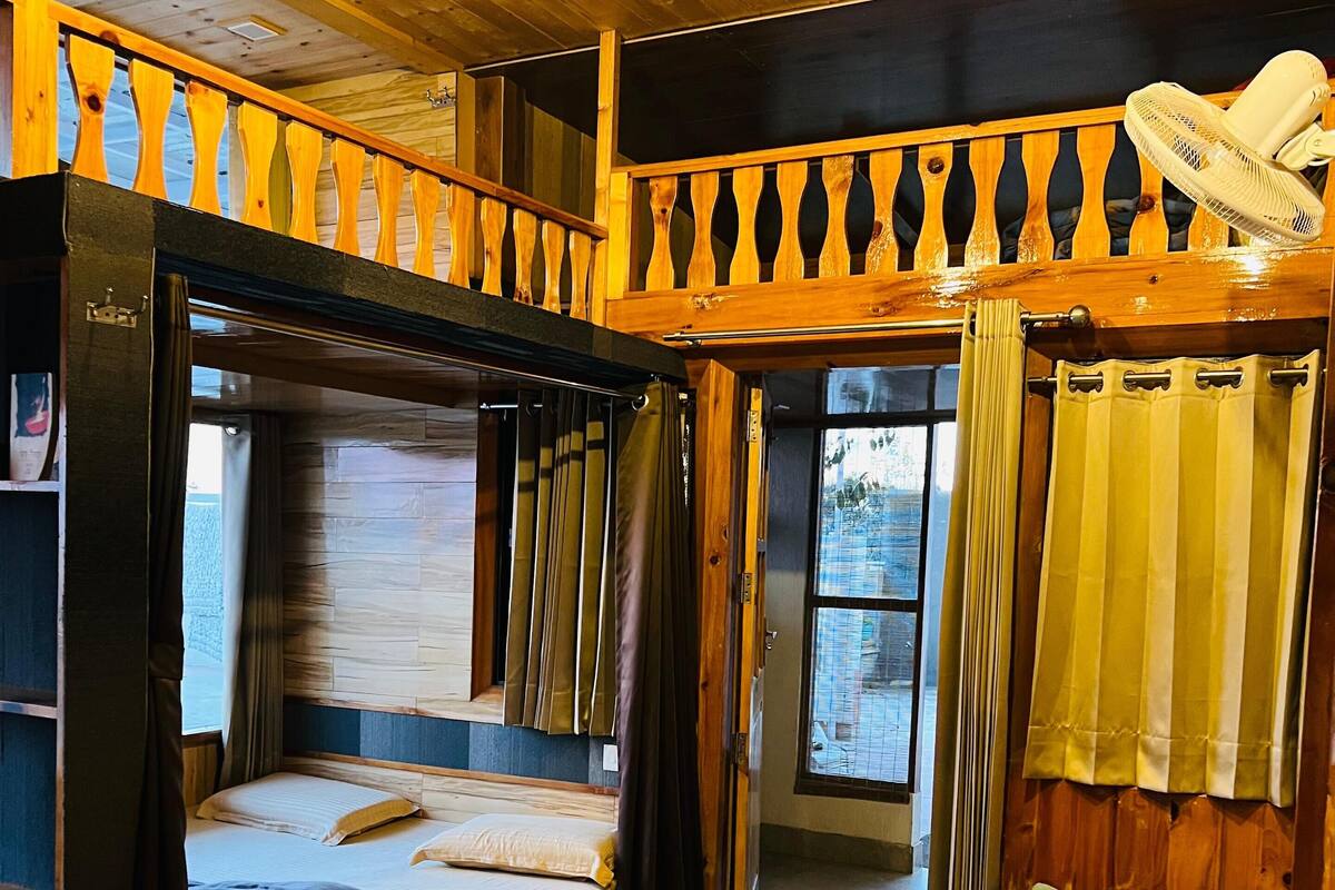 Une pièce avec un lit superposé, un canapé-lit et une petite table. Il y a une fenêtre avec des rideaux, un ventilateur de plafond et un luminaire.