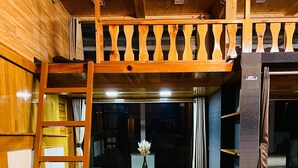 A cozy cabin interior with a loft bed, a wooden bench, and a small table with a vase. - Snooze Cottage (Dhari)