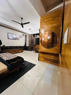 A modern bedroom with a bed, a round mirror, a ceiling fan, and a dining area with chairs and a table. - Snooze Cottage (Dhari)