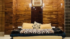 A modern bedroom with a wooden accent wall, a framed picture, and a bed with patterned bedding. - Snooze Cottage (Dhari)