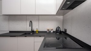 A modern kitchen with white cabinets, a black countertop, a built-in stove, and a stainless steel sink. - RentPlanet - Apartament Kasztelańska (Kraków)
