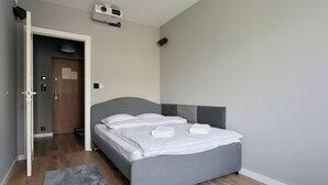 A modern bedroom with a grey bed, a grey headboard, a wooden floor, a grey rug, and a door leading to another room. - RentPlanet - Apartament Kasztelańska (Kraków)