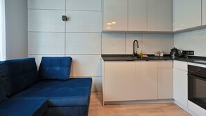 A compact kitchen with white cabinets, a black countertop, and a built-in oven. - RentPlanet - Apartament Kasztelańska (Kraków)