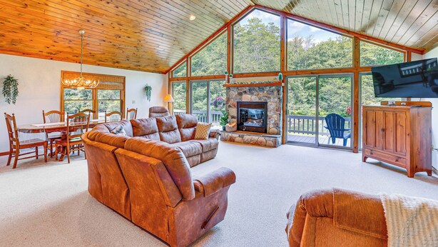 Un salón espacioso con chimenea, techo de madera y amplias ventanas que ofrecen vistas al exterior.
