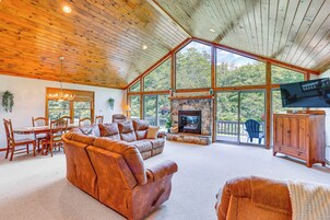 Un salón espacioso con chimenea, techo de madera y amplias ventanas que ofrecen vistas al exterior.