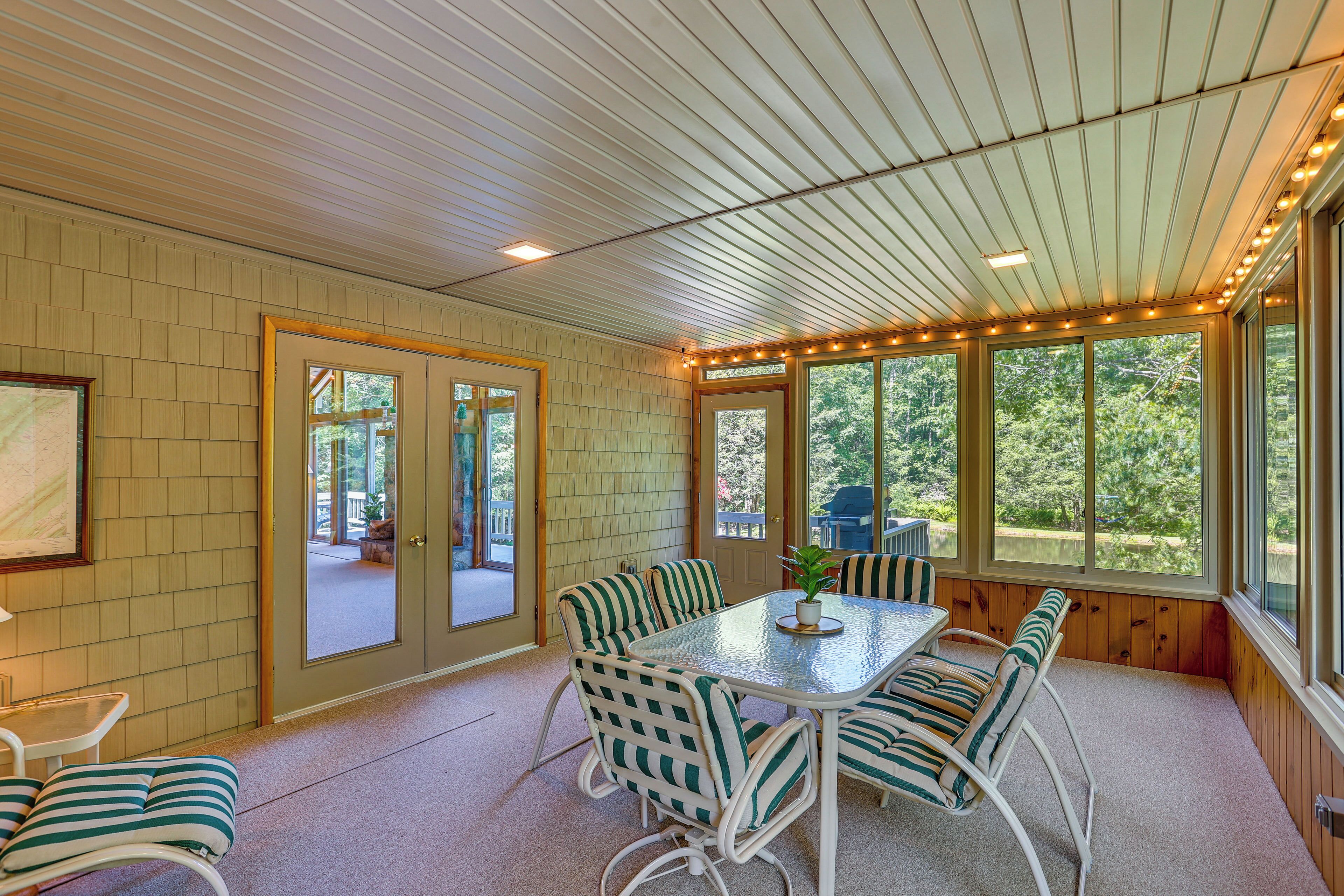 A covered patio with a table and chairs, large windows, and a view of the outdoors.