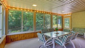 Un patio techado con mesa y sillas, ventanas amplias y vista a árboles.