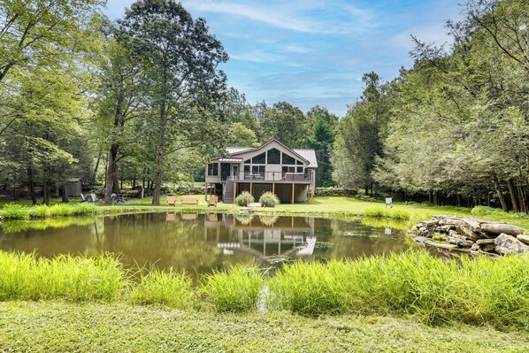 Uma casa com um alpendre amplo, rodeada por um lago e vegetação exuberante.