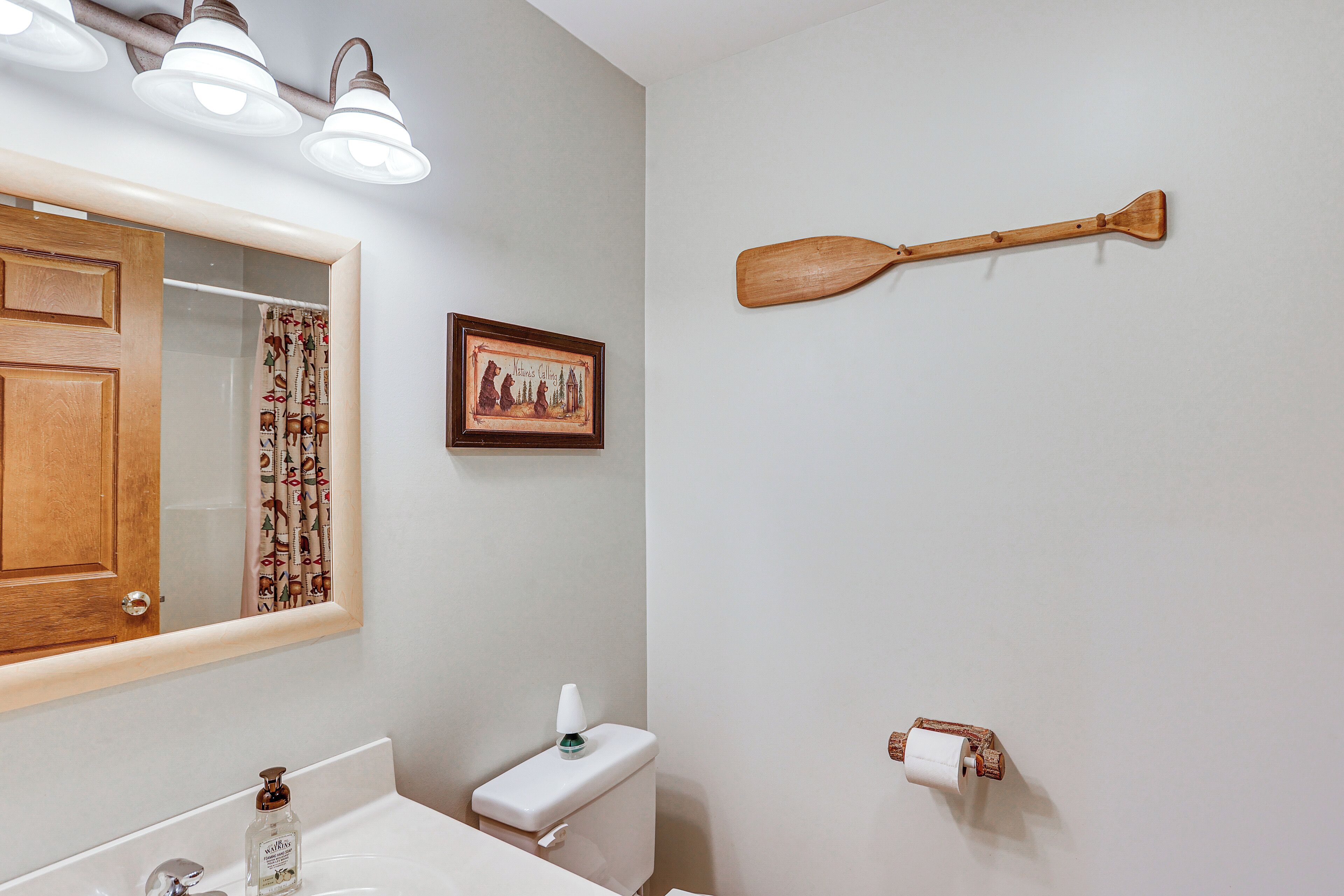 Une salle de bain avec une porte en bois, un miroir, des toilettes, un lavabo et une pagaie en bois accrochée au mur.