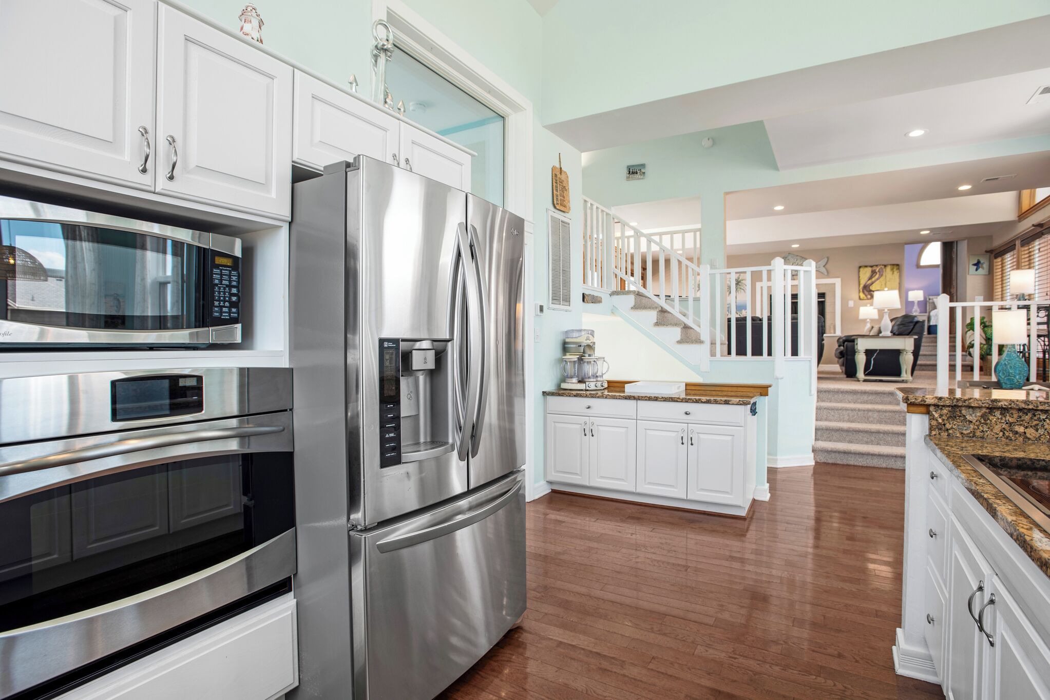 A modern kitchen with stainless steel appliances, white cabinetry, and a wooden floor.