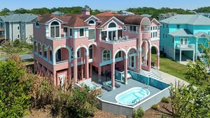 A large, multi-story house with a swimming pool, multiple balconies, and a spacious backyard. - Tickled Pink: Pool | Hot Tub | Elevator | Dogs OK (Corolla)