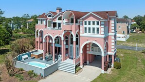 A large, multi-story house with a swimming pool, arched windows, and a balcony. - Tickled Pink: Pool | Hot Tub | Elevator | Dogs OK (Corolla)
