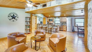 A spacious living area with leather sofas, a coffee table, and a fireplace. A kitchen is visible in the background with modern appliances and a stone accent wall. - Deck & Fire Pit: Unique Pottsboro Haven (Pottsboro)