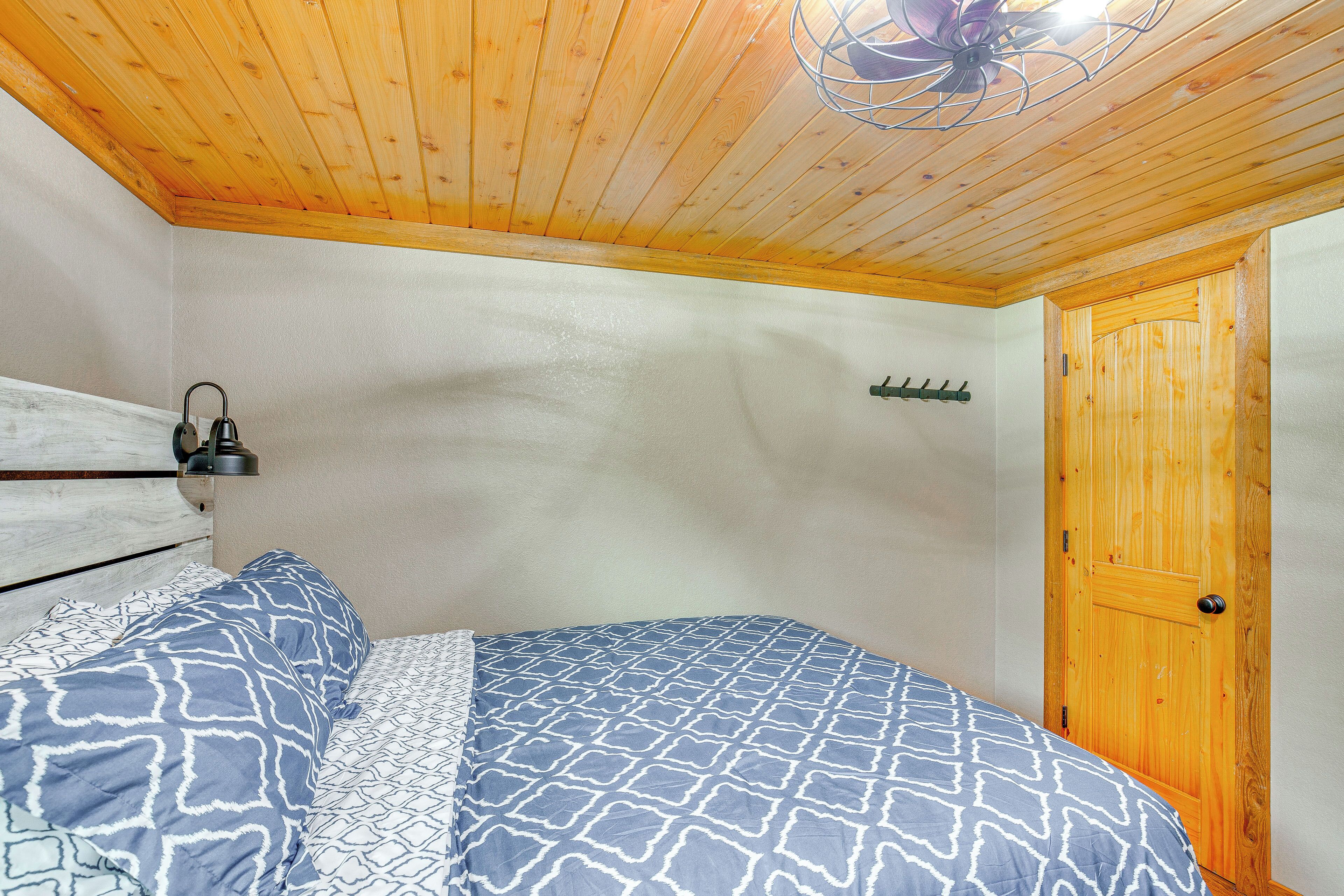 Un dormitorio con techo de madera, una cama con ropa de cama estampada, una lámpara de pared y una puerta de madera.