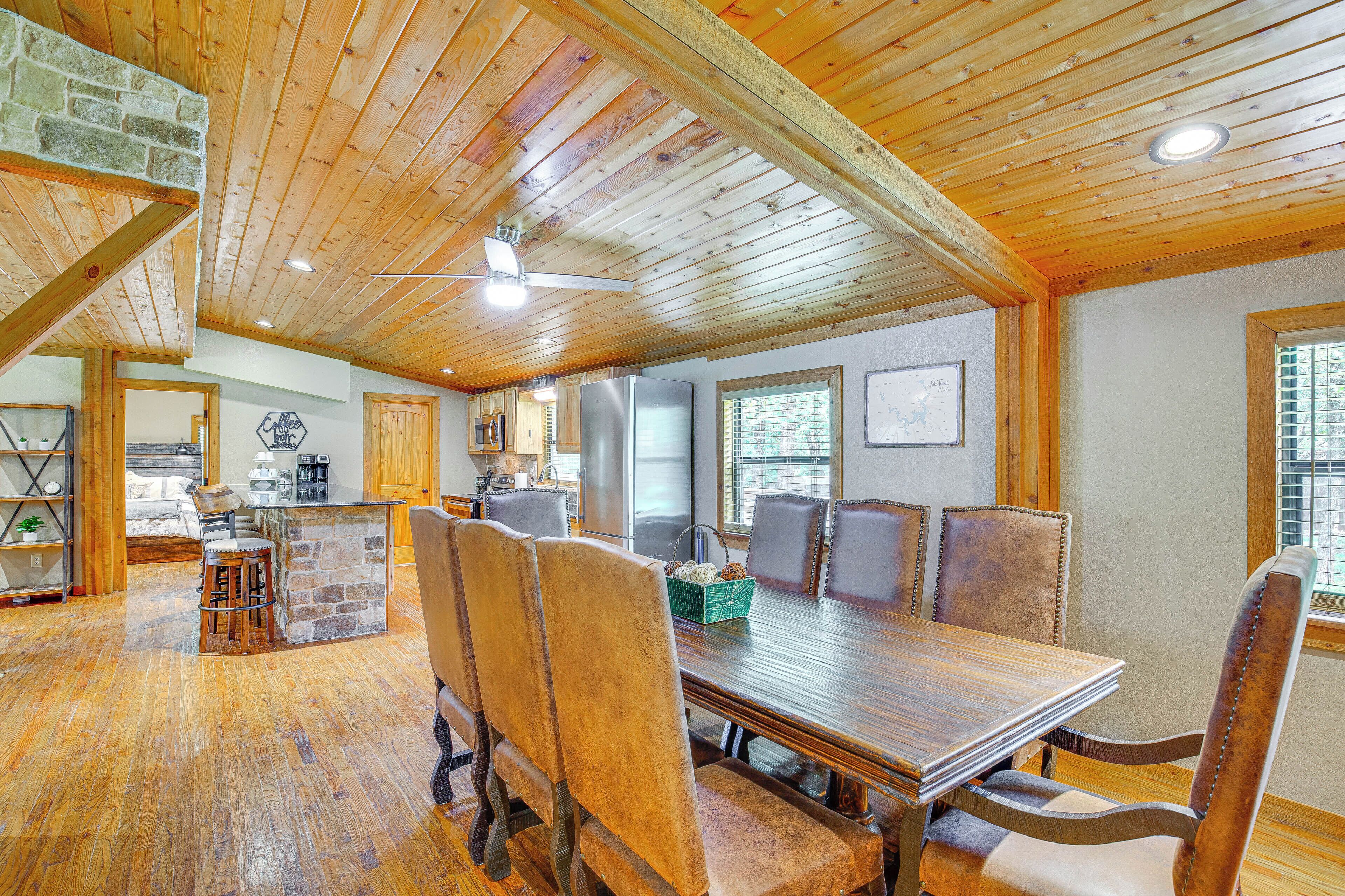 Un comedor espacioso con una mesa y sillas de madera, un muro decorativo de piedra y una cocina al fondo.
