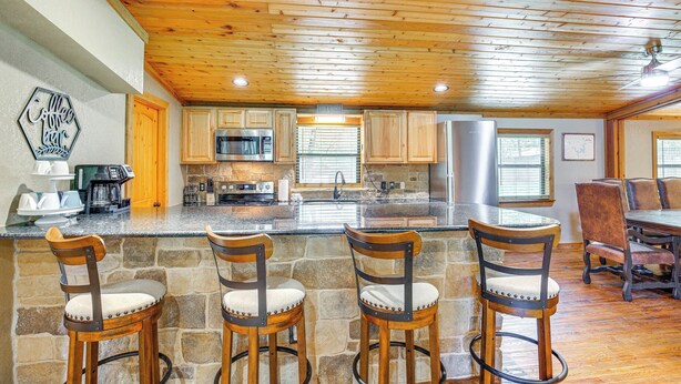 A kitchen with stone countertops, wooden chairs, and a stone wall. - Deck & Fire Pit: Unique Pottsboro Haven (Pottsboro)
