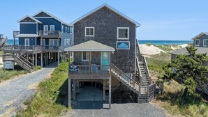 Een pand aan het strand met een houten gebouw, een overdekte veranda en een trap naar een terras.