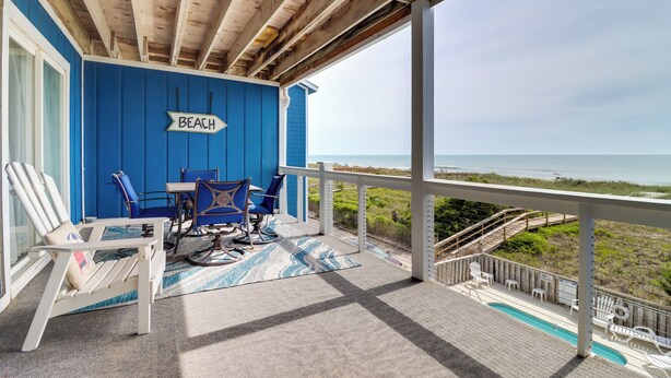 Un espace extérieur abrité, avec vue sur la plage, comprenant un mur bleu, une enseigne indiquant « PLAGE » et du mobilier d’extérieur.