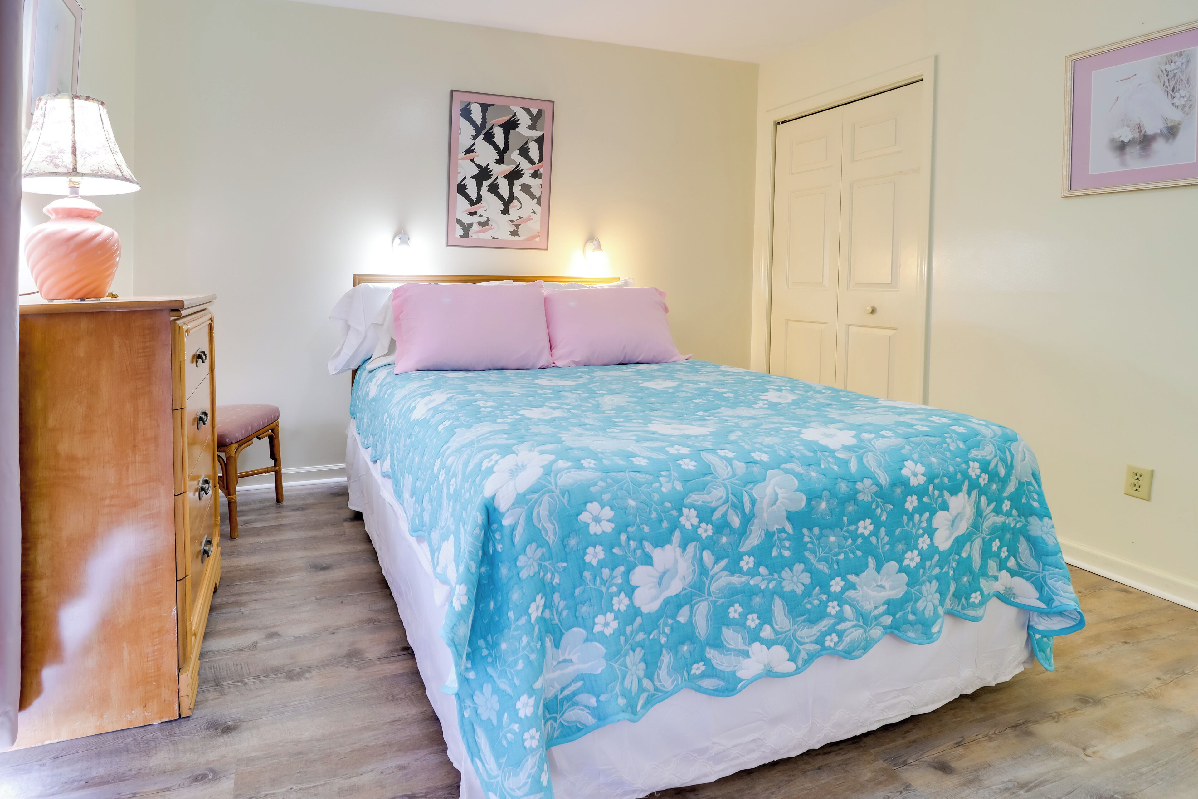 A bedroom with a bed, a wooden dresser, a chair, and a wall-mounted lamp.