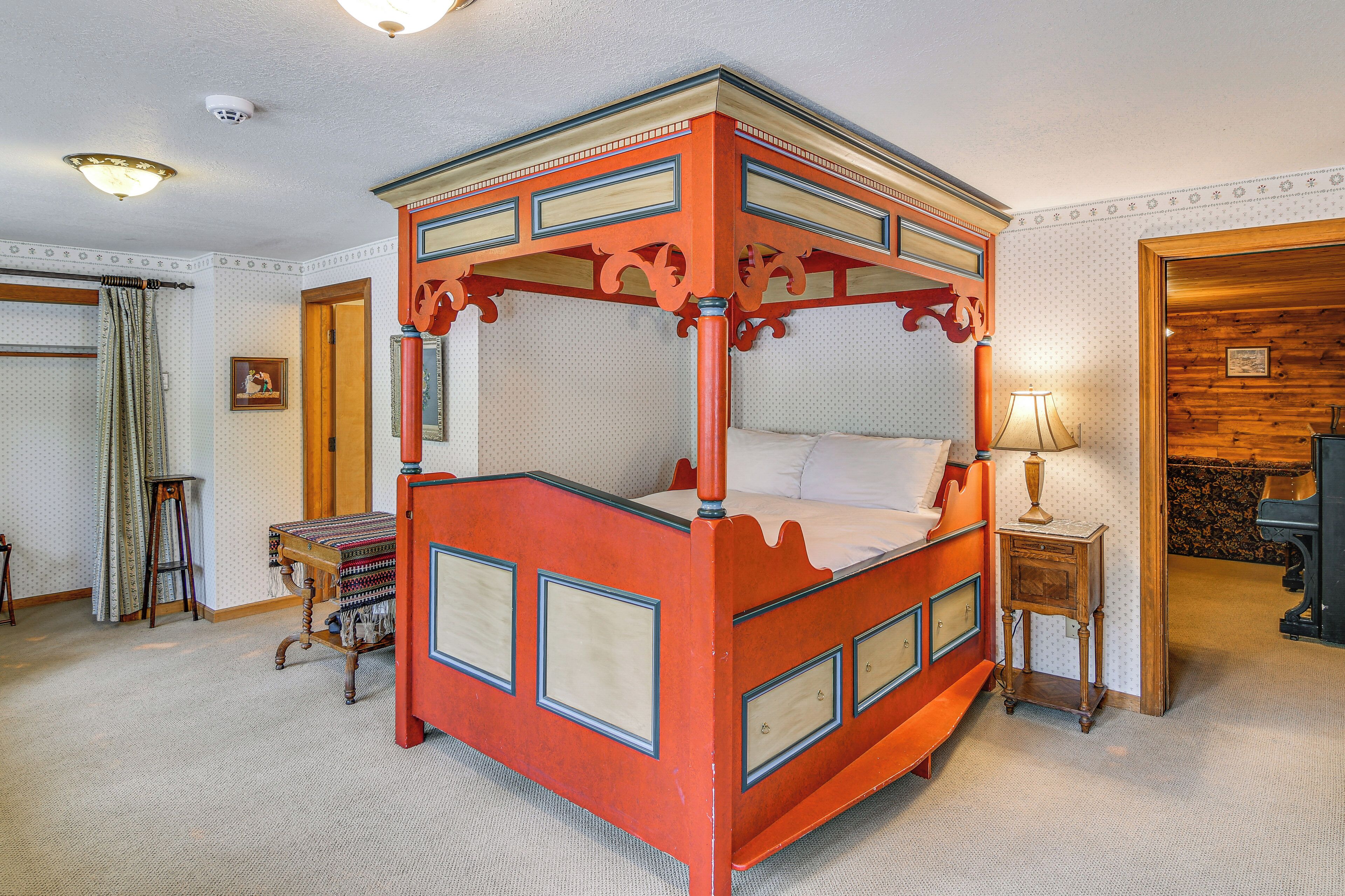 Un lit à baldaquin avec une structure en bois et un ciel de lit, une table de chevet avec une lampe, et un tapis à motifs.