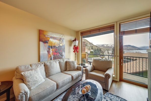 A living room with a sofa, armchair, and a coffee table. There is a painting on the wall and a view of a balcony with a railing. - Pool, Hot Tub, & Beach Access! Chelan Family Haven (Chelan)