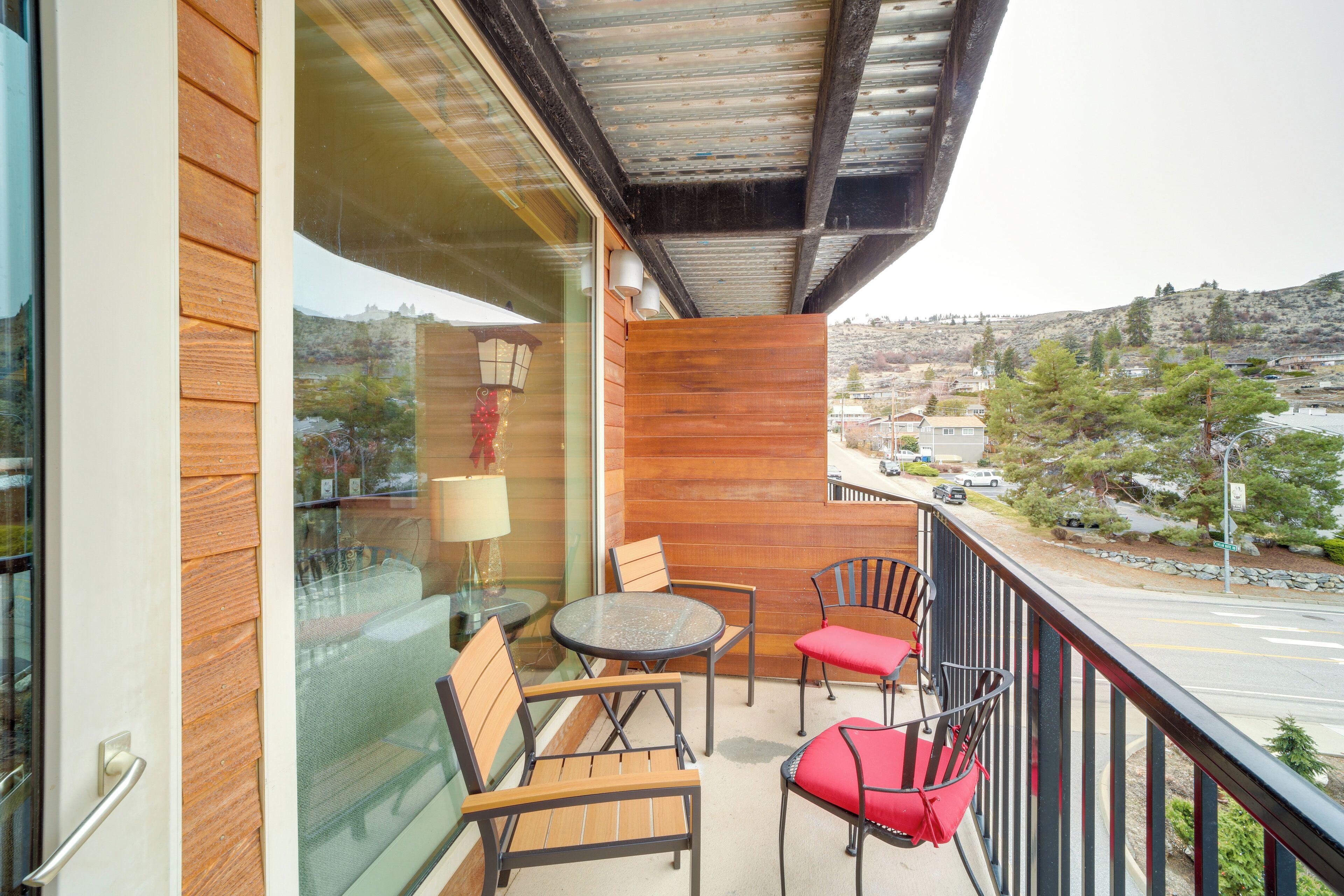 A balcony with wooden furniture, a glass door, and a view of a town.