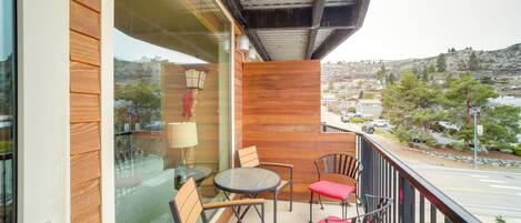 A balcony with wooden furniture, a glass door, and a view of a town.