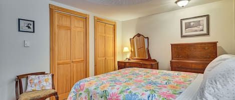 Un dormitorio con colcha estampada, armario de madera, una silla, cómoda y una lámpara en el techo.
